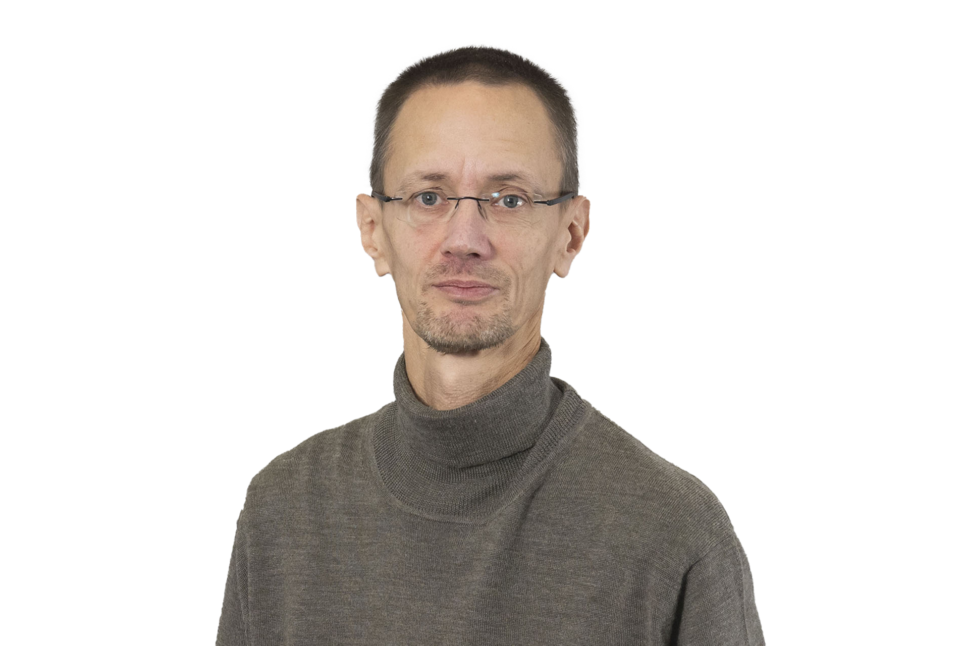 Porträt eines Mannes mit kurz geschnittenem Haar, Brille und grauem Rollkragenpullover. Er blickt neutral in die Kamera. Der Hintergrund ist grau.